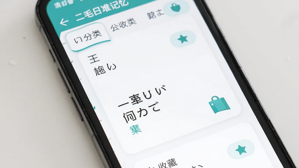 二毛日语单词记忆界面,主体为手机屏幕显示场景分类与单词卡片,布局为列表加卡片式,排版简洁,风格日系清新,细节包含单词、假名、中文释义和收藏按钮,画质清晰,干净,无多余元素