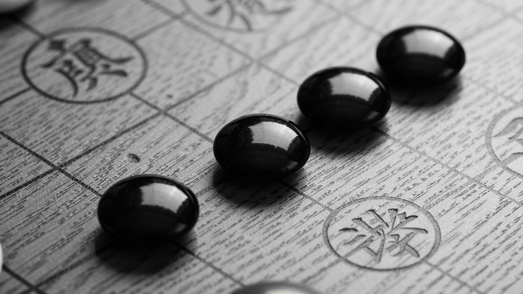 主体为一副黑白五子棋对局特写,五枚黑色棋子沿对角线整齐连成一线,布局采用斜向引导线构图,视觉焦点集中在连珠位置,排版上棋盘局部放大占据画面八成区域,风格为写实棋类摄影质感,细节呈现棋子表面细腻的釉面反光与木纹棋盘纹理,画质高清,画面干净,无多余元素