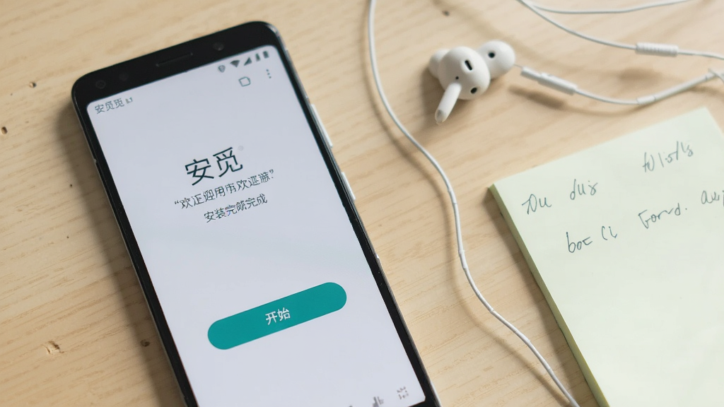 一部安卓手机屏幕显示安觅应用安装完成后的首次打开界面,界面简洁有欢迎语和开始按钮,手机旁放着耳机和便签纸,背景为浅色桌面,画面中可见“安觅”字样,风格清新自然,画质清晰,无杂乱元素