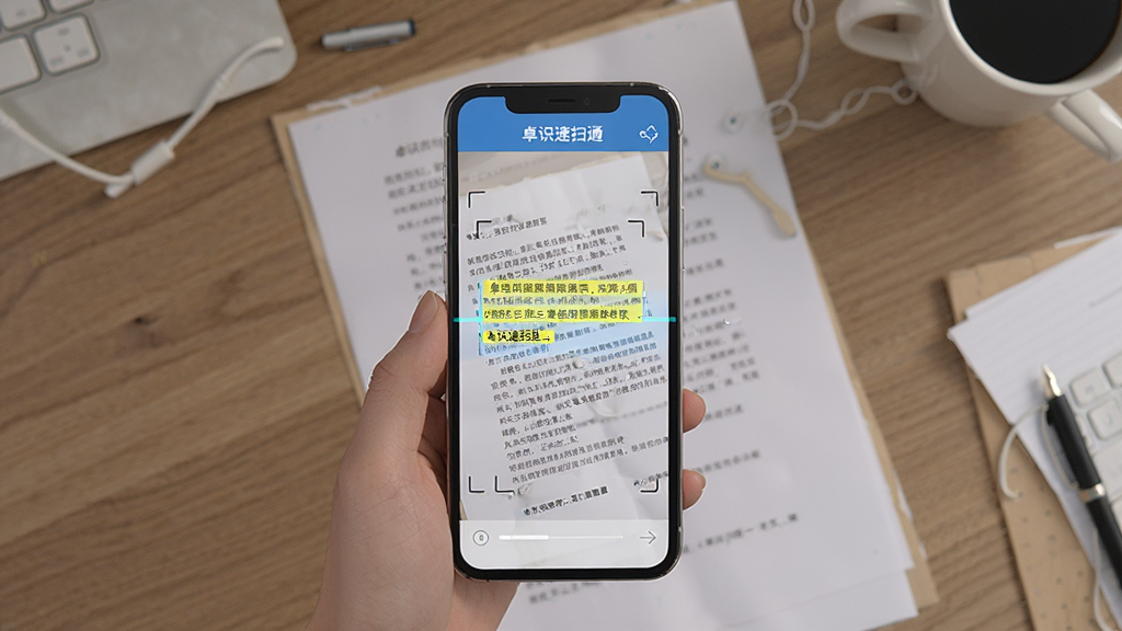 主体为手机扫描纸质文档的俯视画面,屏幕中出现文字高亮选中效果,背景为办公桌面,排版简洁,风格写实,细节展现文字识别与复制功能,画质干净,文字“卓识速扫通”出现在手机界面顶部。
